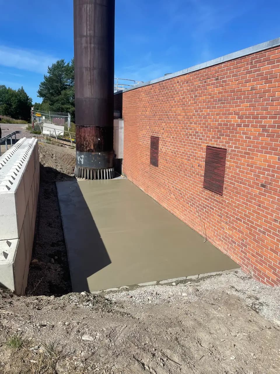 Nygjuten betongyta vid tegelbyggnads fasad