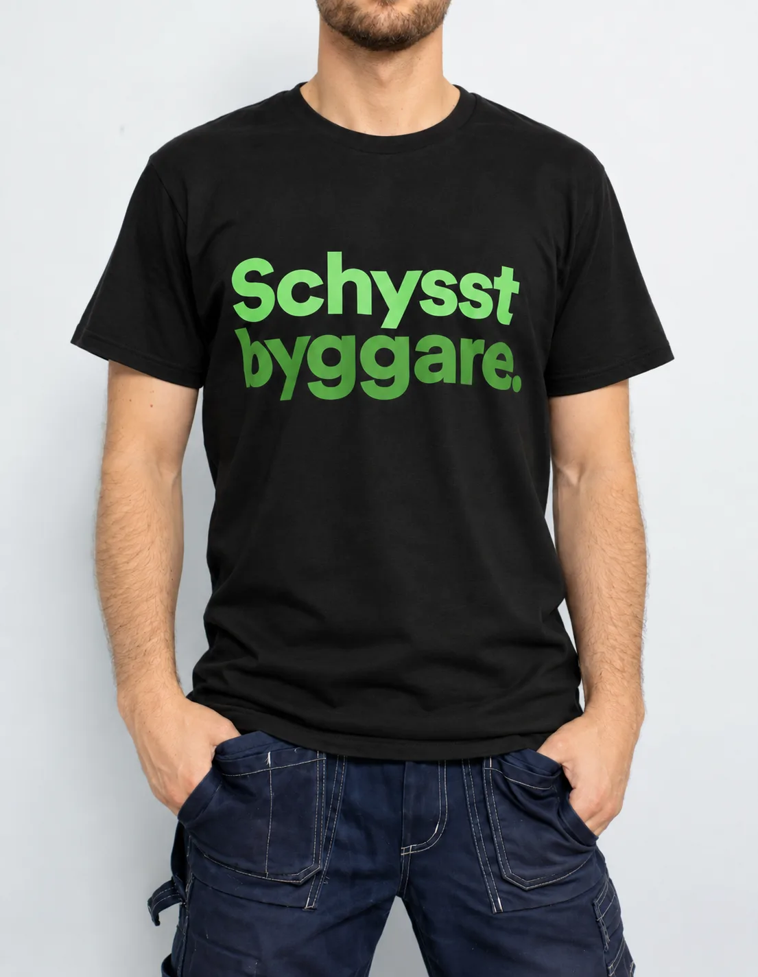 Byggare i svart t-shirt med texten ”Schysst byggare.” i grönt